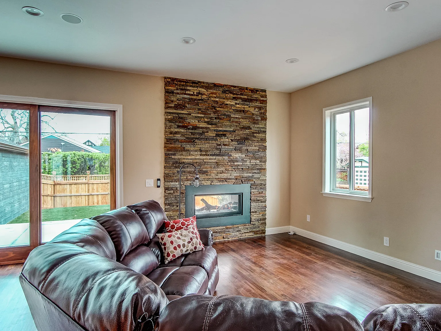 Cozy living room with hardwood floors, stone fireplace, and large windows offering natural light