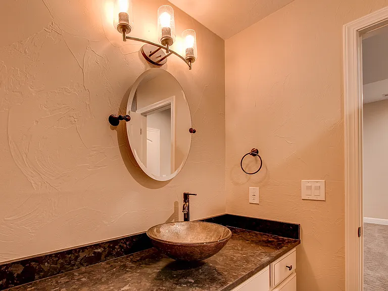 Powder room with textured walls, round mirror, and striking vessel sink on dark granite countertop