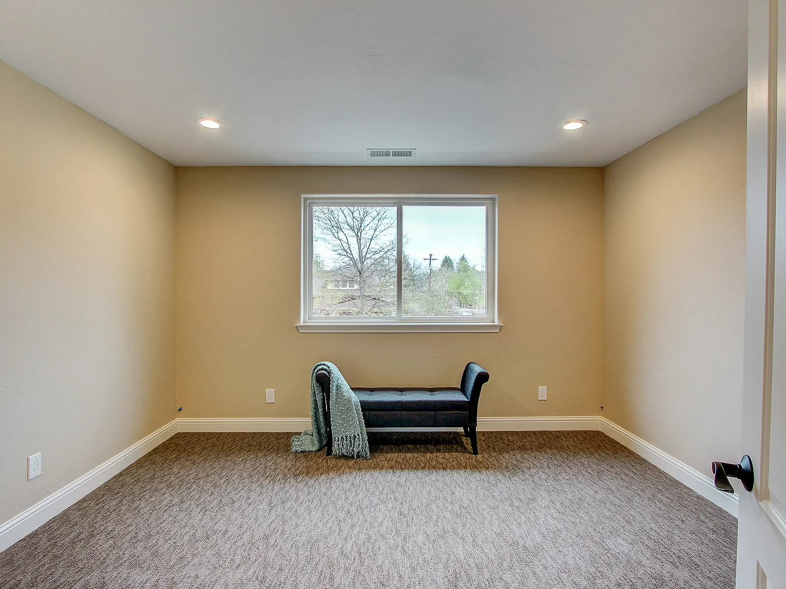 Cozy carpeted bonus room or den with recessed lighting and central window view