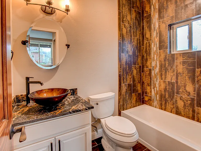 Stylish powder room with vessel sink, granite countertop, and circular mirror framed by wall sconces
