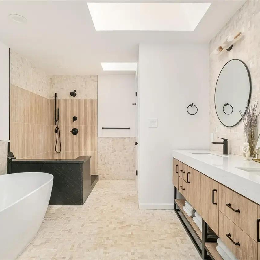 Contemporary bathroom with freestanding white soaking tub, walk-in shower with black fixtures, dual vanity with wood cabinetry and vessel sinks, round mirrors, and neutral tile walls and floors.