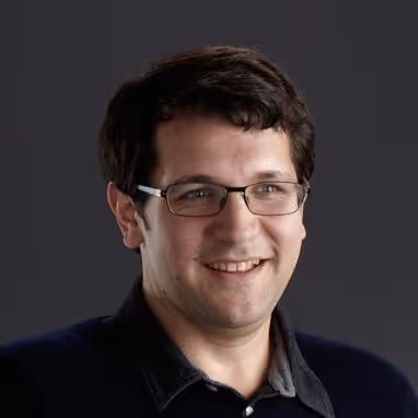 Headshot of Dion Almaer, VP of Product at Augment, wearing glasses and smiling against a dark background.