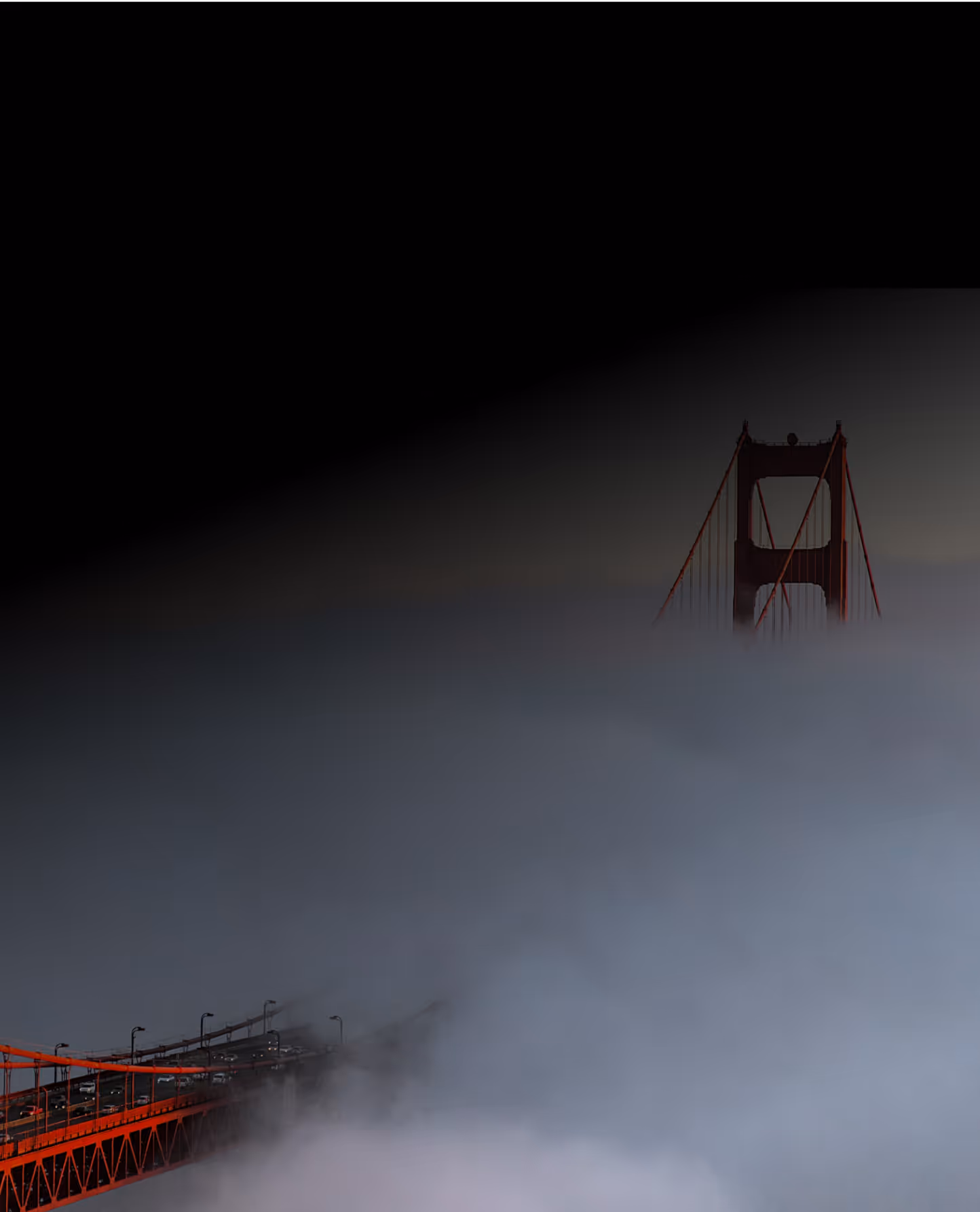 Golden Gate Bridge partially covered in fog with only the tops of the towers visible against a dark sky.