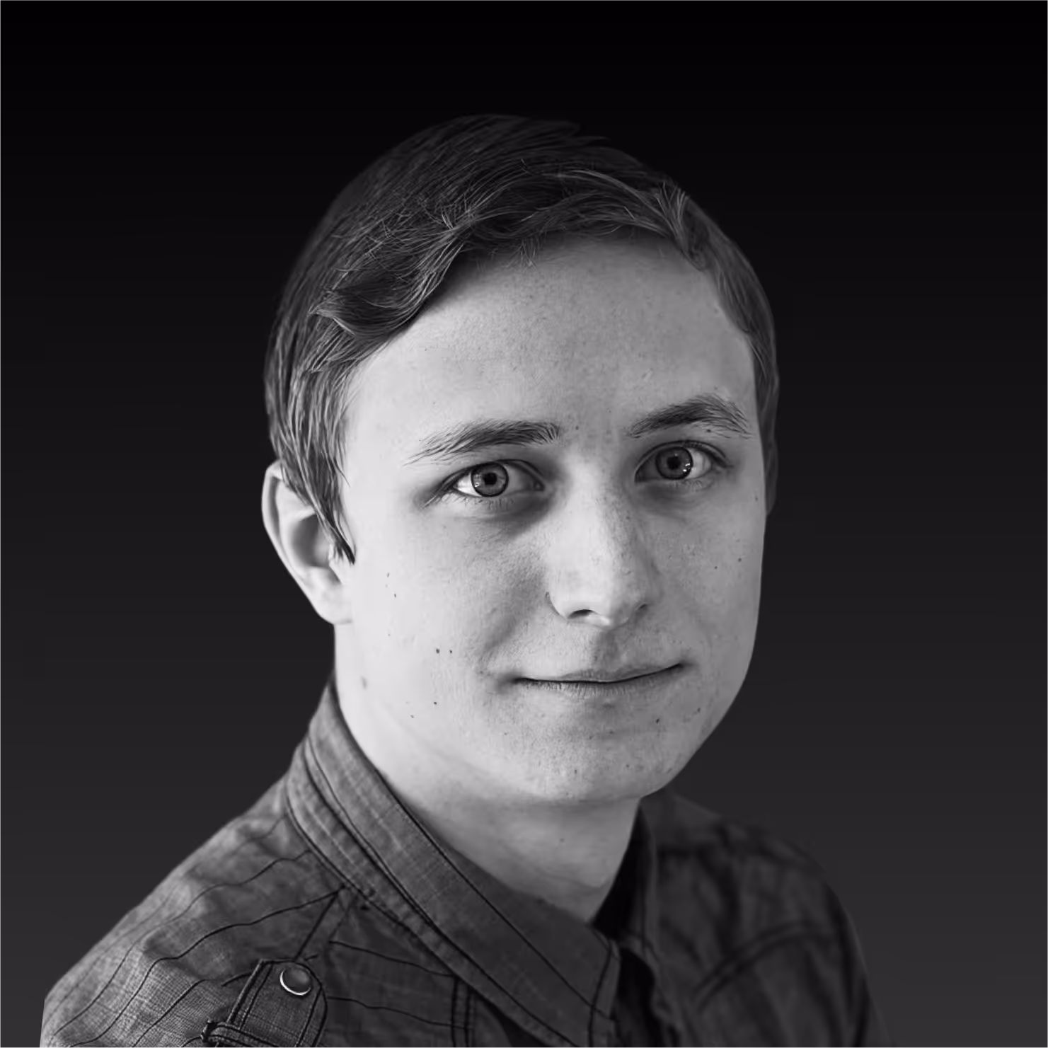 Black and white close-up portrait of a young man with short hair wearing a plaid shirt against a dark background.