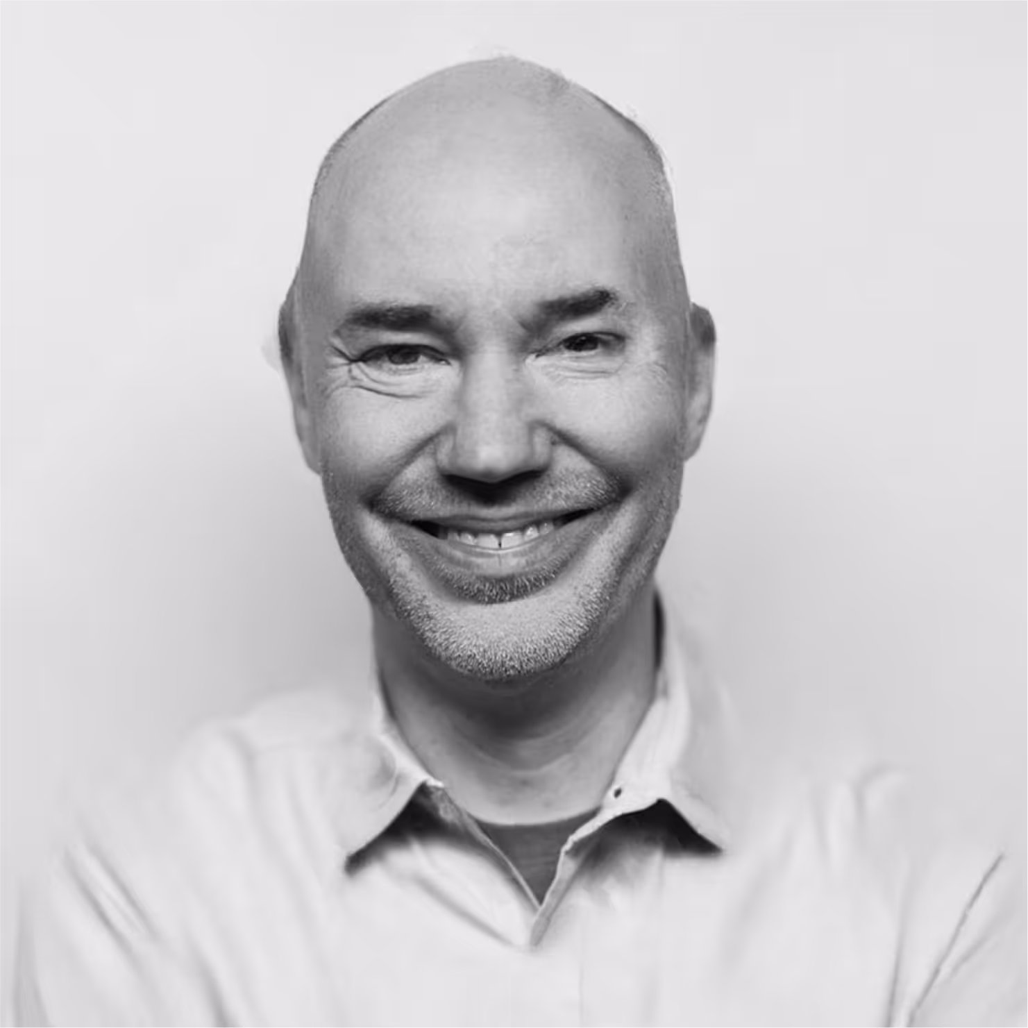 Smiling middle-aged bald man with facial hair wearing a collared shirt against a plain background.
