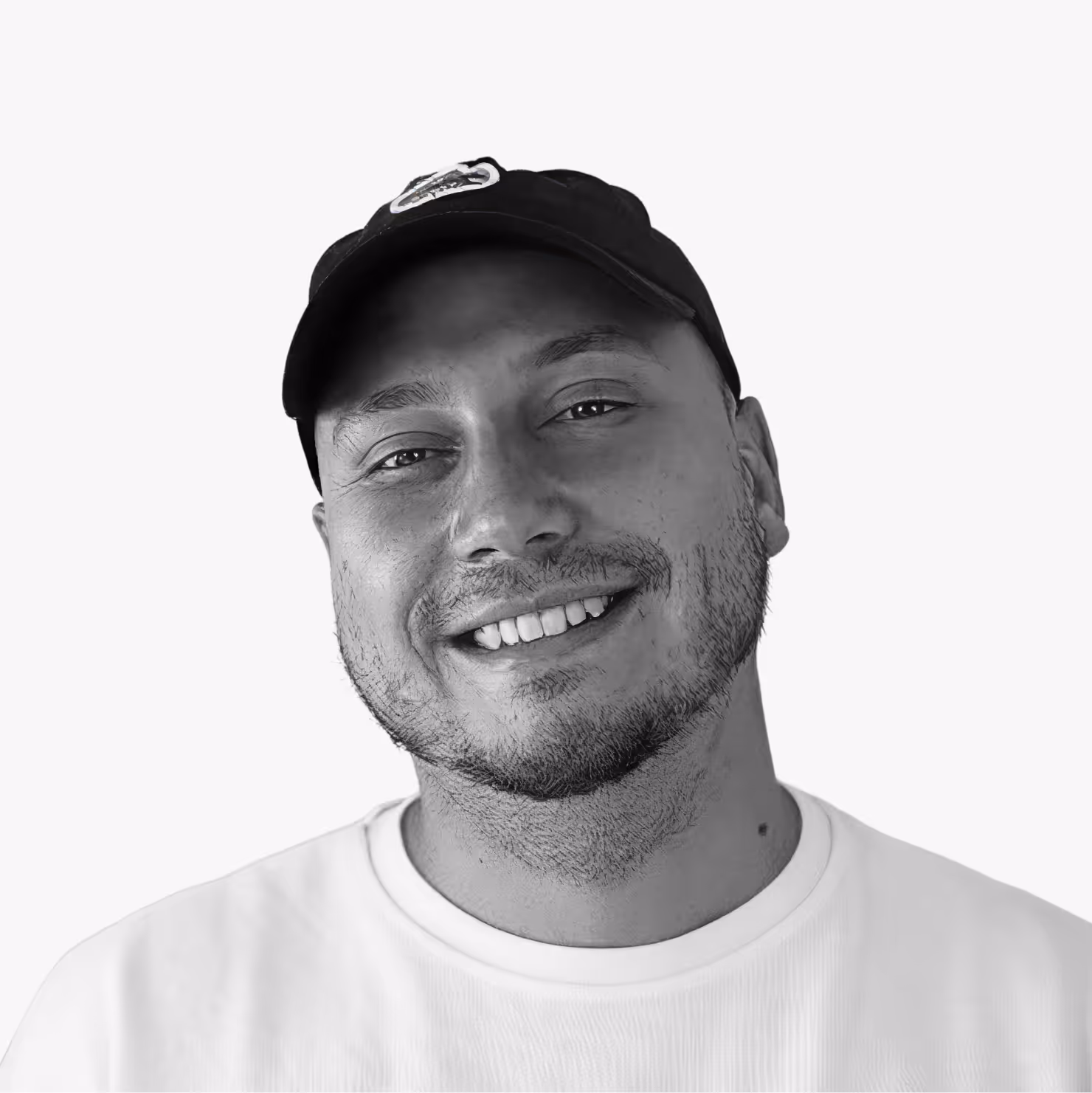 Smiling man wearing a black baseball cap and white shirt against a plain background.