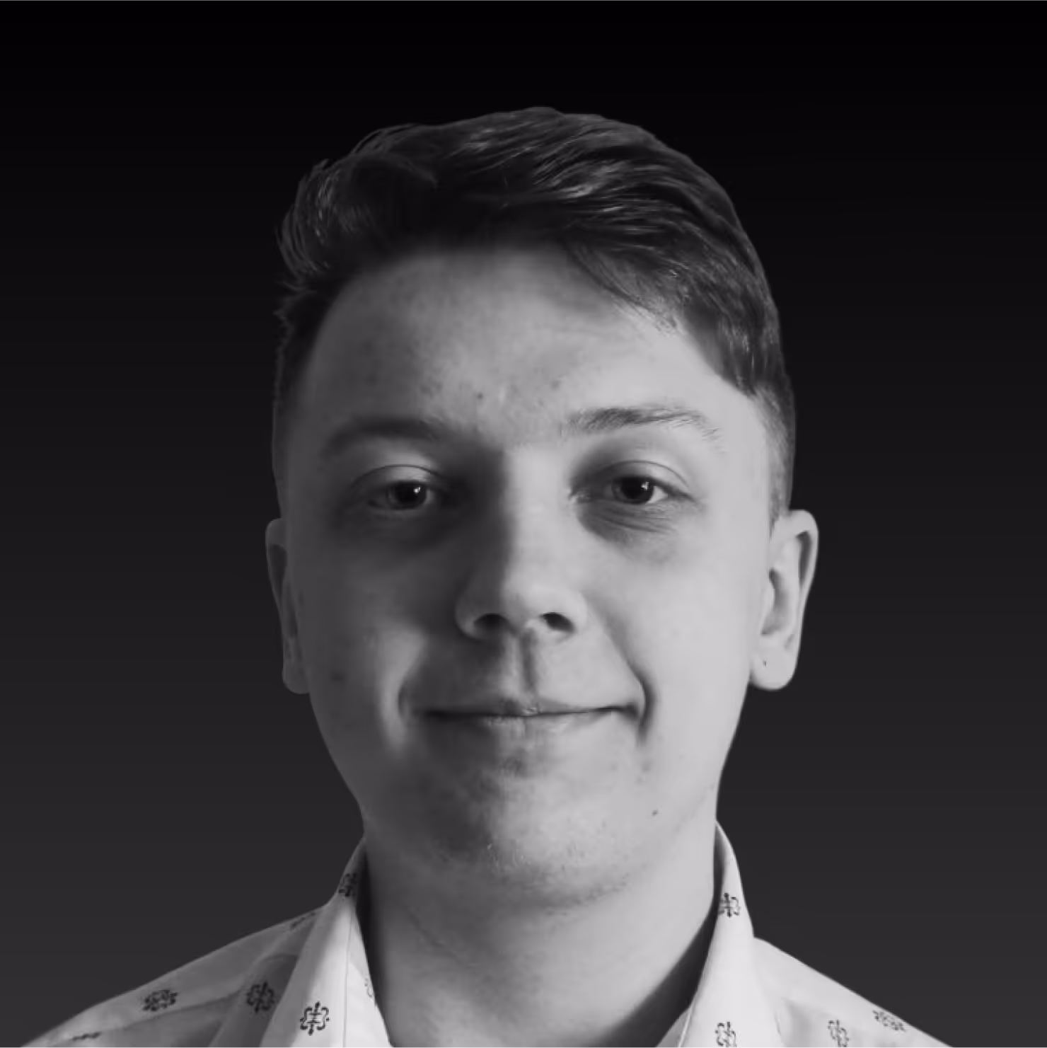 Black and white close-up portrait of a young man with short hair smiling slightly against a dark background.