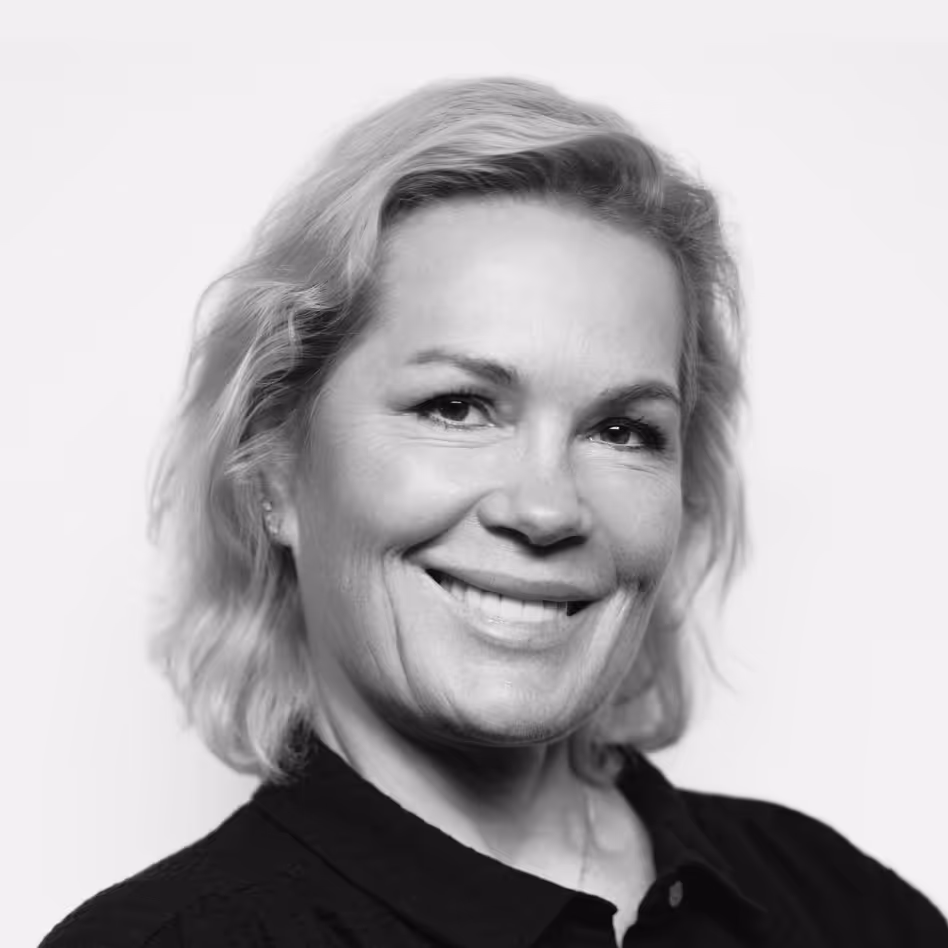 Smiling middle-aged woman with shoulder-length wavy blonde hair wearing a black top against a plain background.