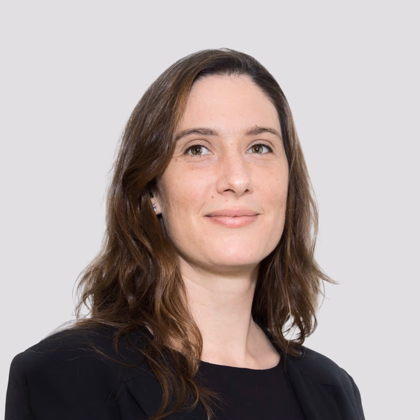 Smiling woman with shoulder-length brown hair wearing a black blazer and top, against a light gray background.