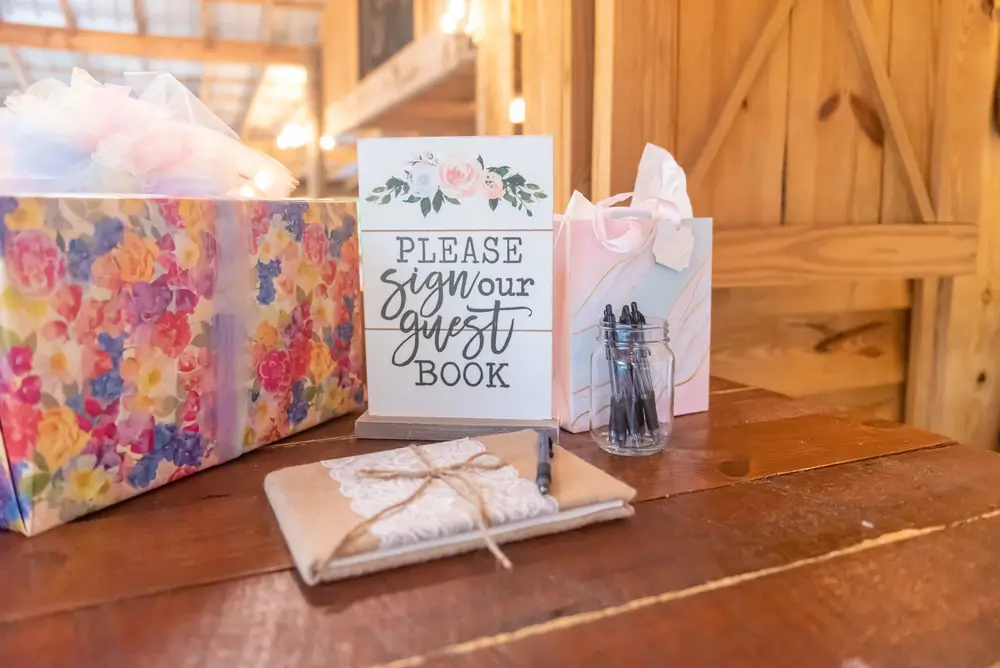 Traditional physical wedding guest book setup with pens, cards, and a guest book sign.
