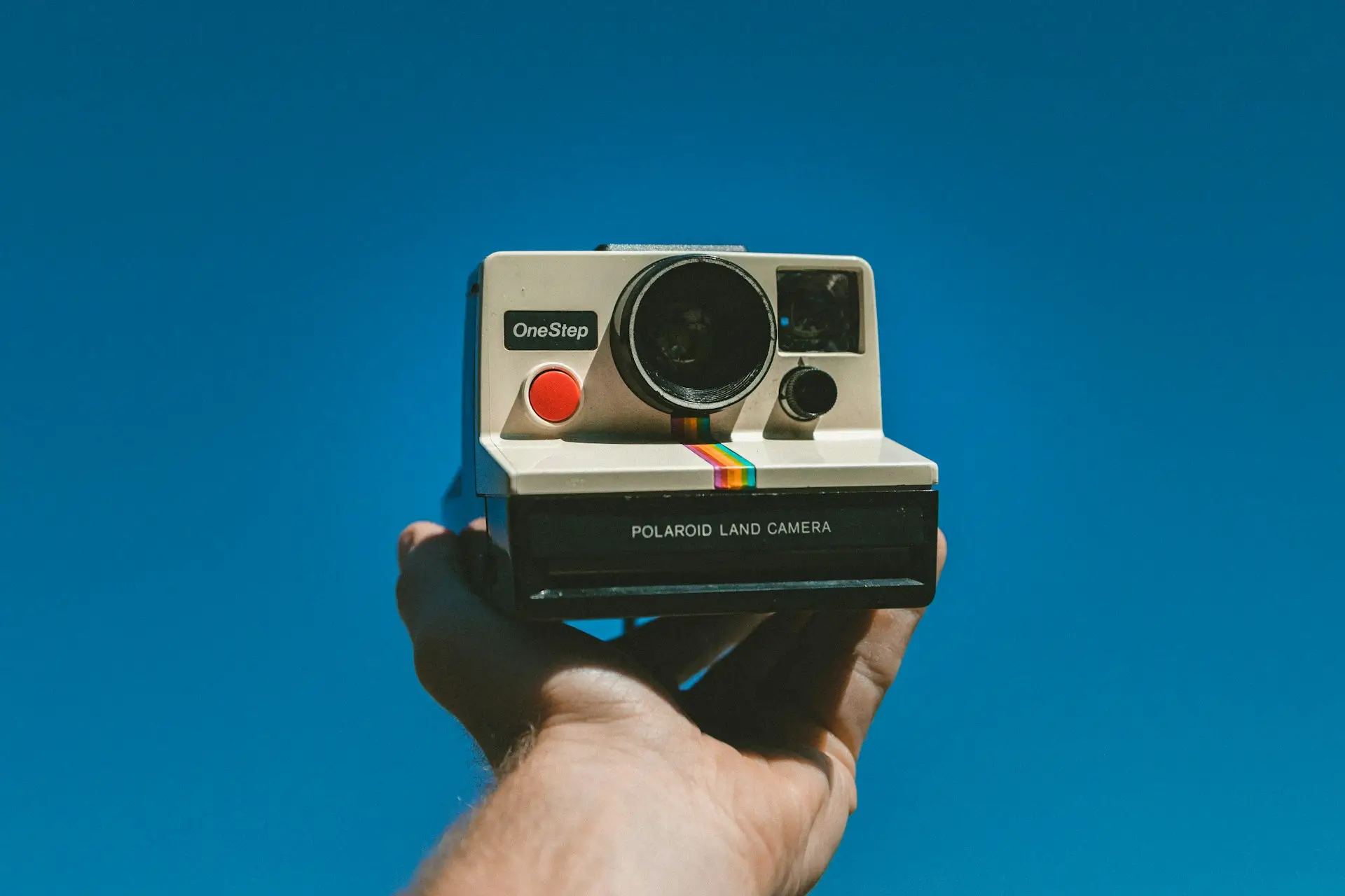 Classic Polaroid OneStep instant camera held up against a clear blue sky background.