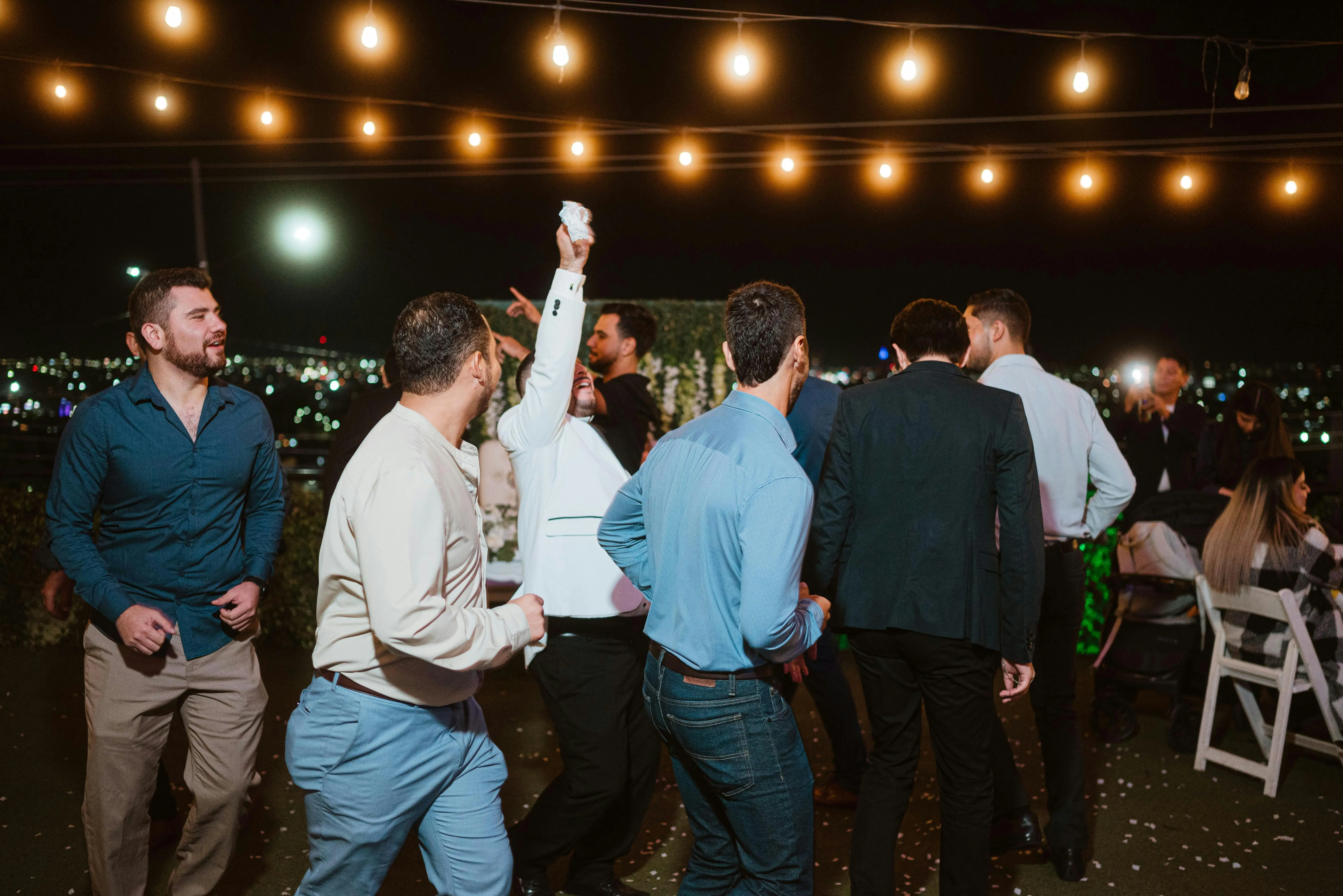Wedding guests dancing at an outdoor reception under string lights.