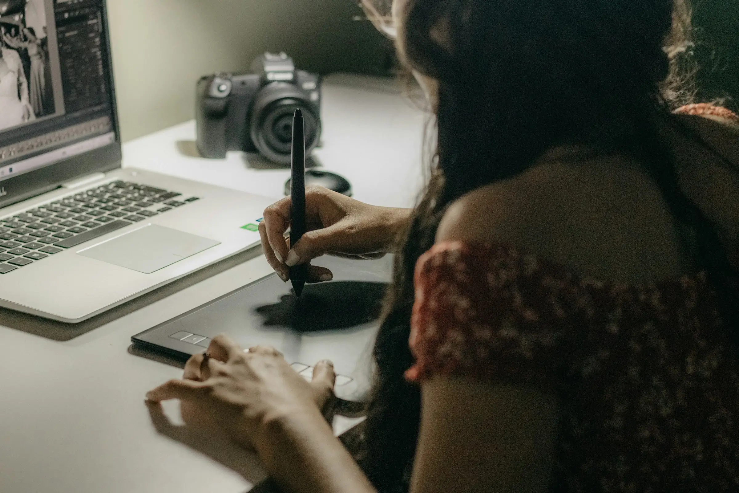 Photographer editing photos on a laptop with a camera beside her.
