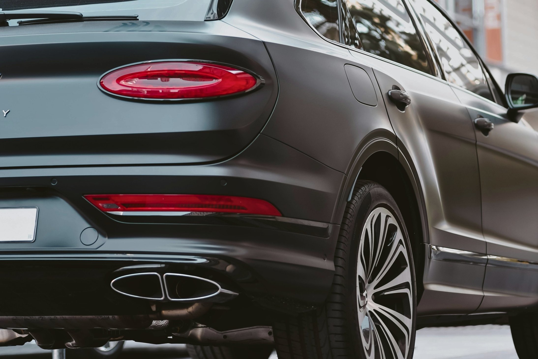 Close-up of the rear side of a matte black luxury SUV showing the tail light, exhaust pipes, and rear wheel.
