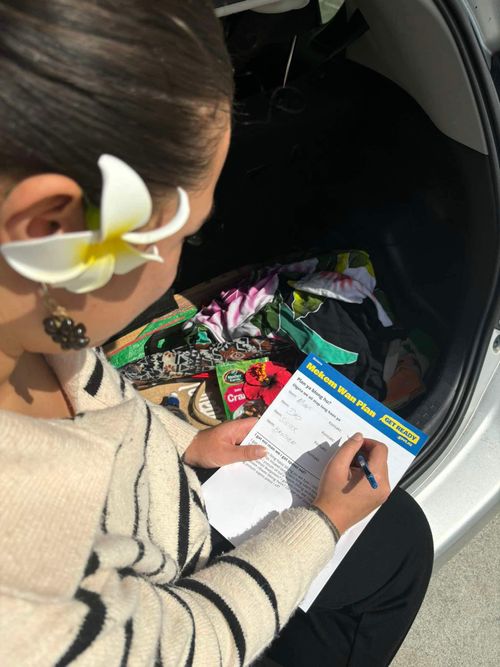 An over the shoulder shot of Nele in the car with a frangipani behind her ear, holding a "Get Ready" plan in front of her.