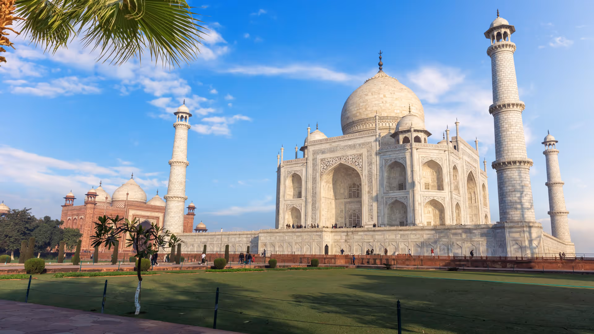 The Taj Mahal in Agra, India, with its white marble dome, minarets, and surrounding gardens under a blue sky.