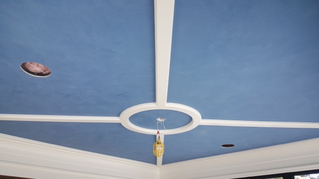 Ceiling painting in progress with a light blue paint and strong contrasting white details on elements of the ceiling.