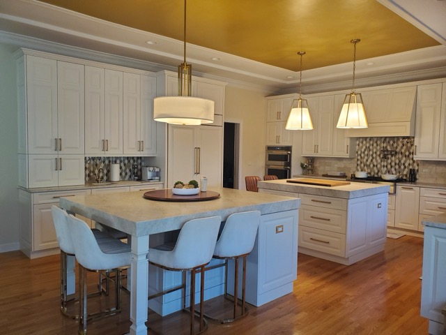 Spacious luxury kitchen remodel by Chris Painting and Remodeling with white shaker cabinetry, large marble island, gold-accented ceiling, brass pendant lights, and geometric tile backsplash