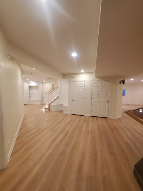 Spacious finished basement remodel by Chris Painting and Remodeling with light hardwood flooring, vaulted tray ceiling, recessed lighting, open layout, staircase, and multiple white paneled doors