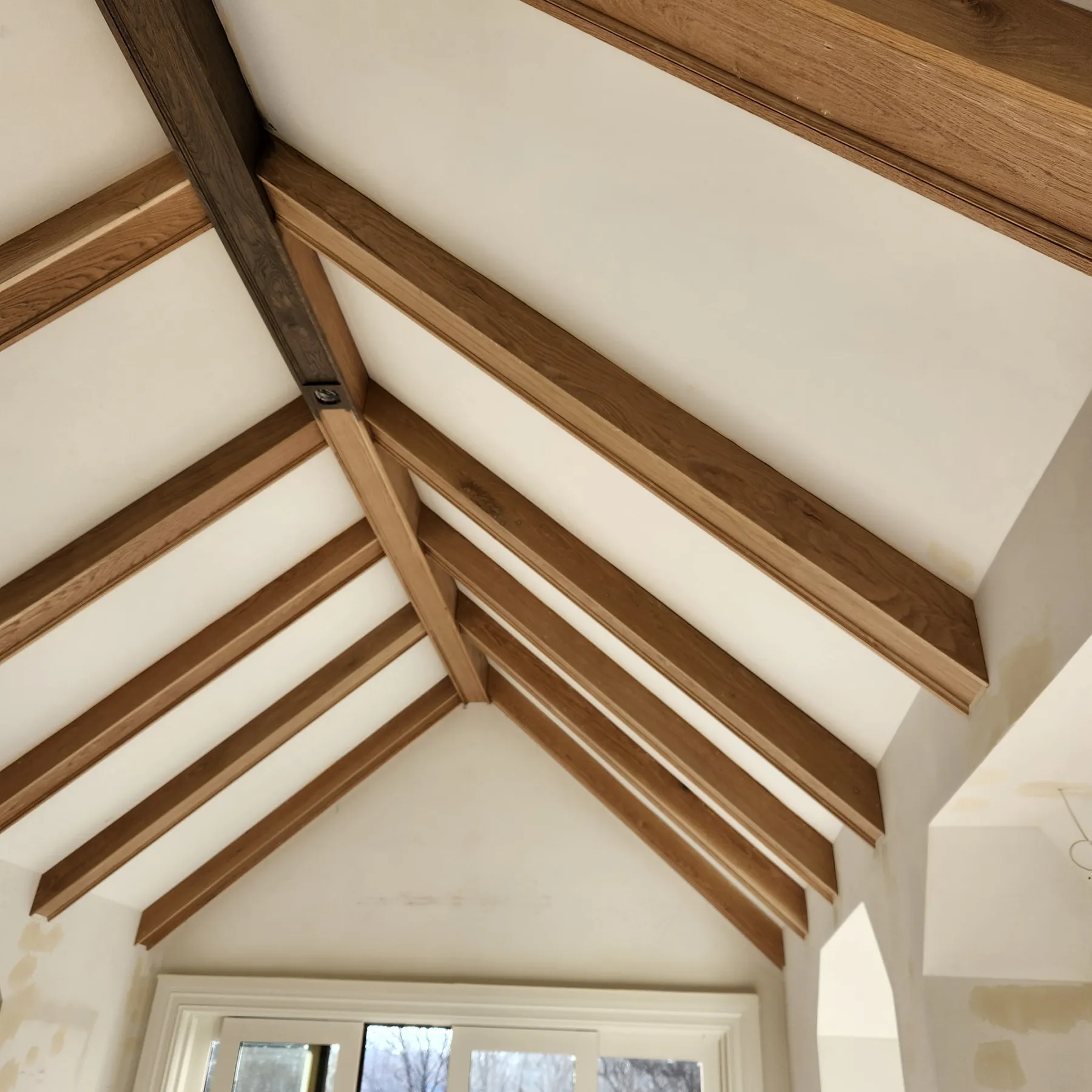 Finished vaulted ceiling featuring stained oak wooden beams in a symmetrical crisscross pattern, crafted by Chris Painting and Remodeling.