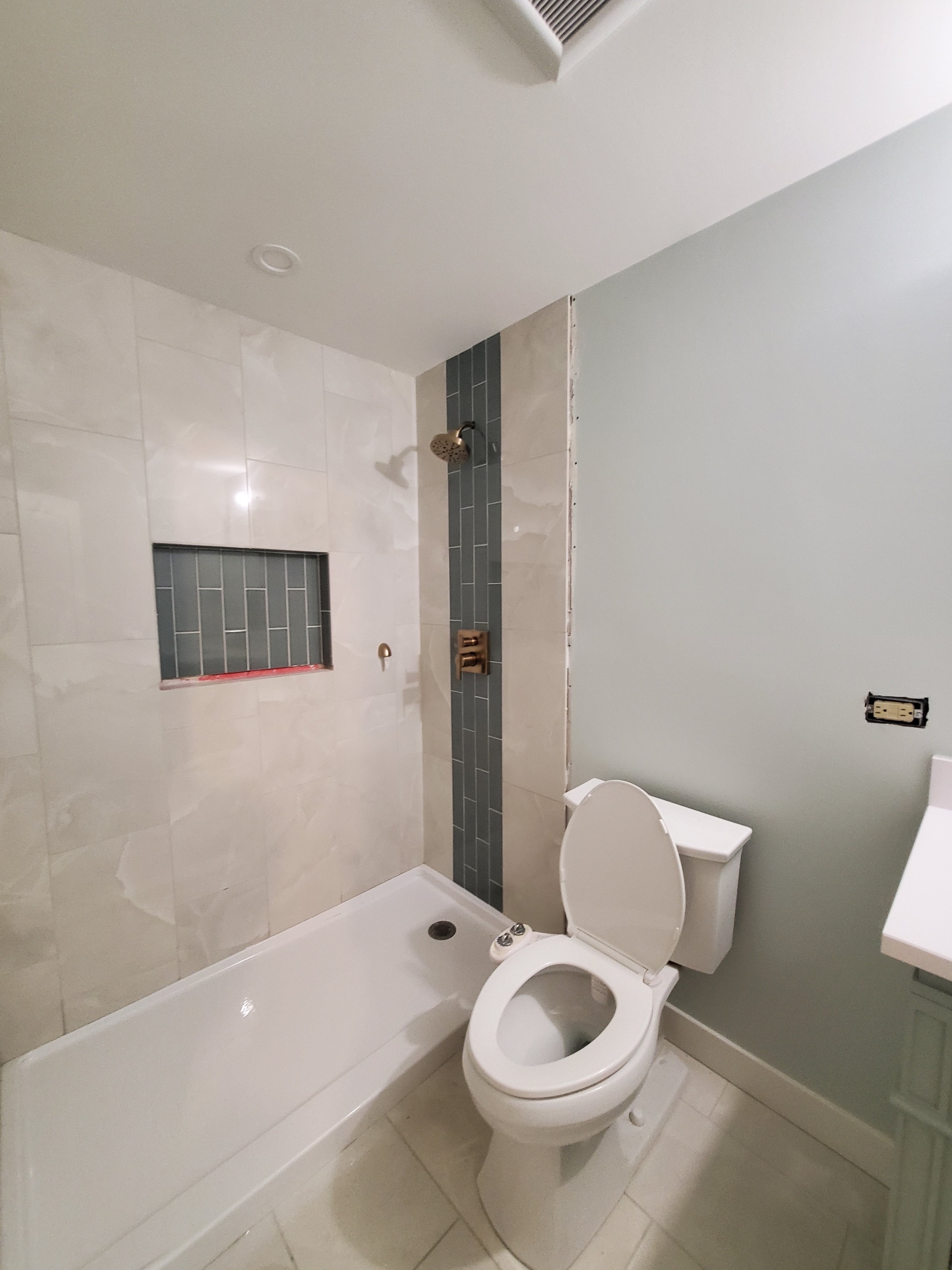 Master bathroom featuring a walk-in shower with a vertical dark subway tile accent strip, frameless glass niche window, rainfall showerhead, freestanding tub, and matching sage-green vanity during remodel by Chris Painting and Remodeling.