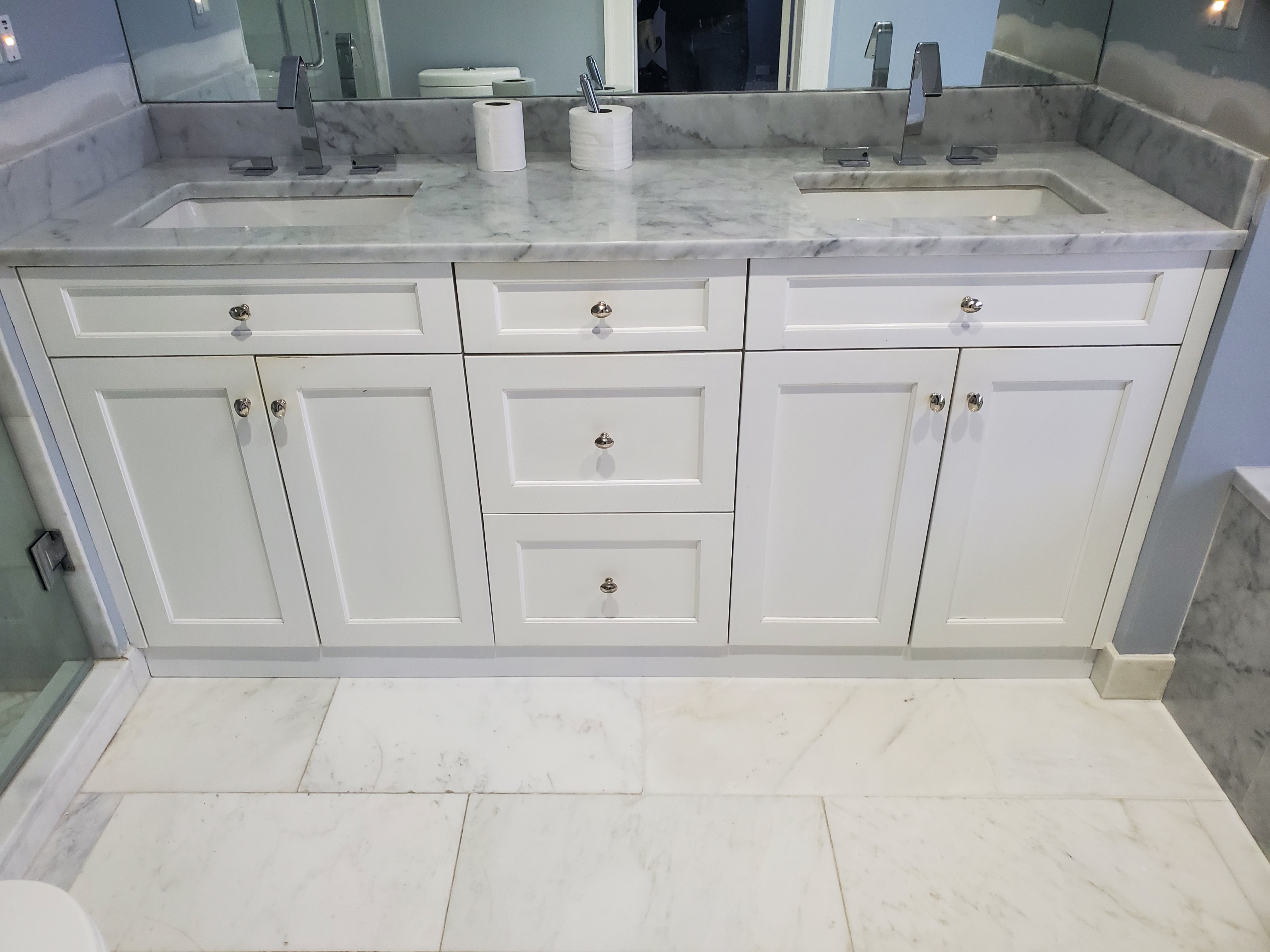 Double vanity with white shaker cabinetry, Carrara marble countertop, dual undermount sinks, chrome angular faucets, and marble tile floor installed by Chris Painting and Remodeling.