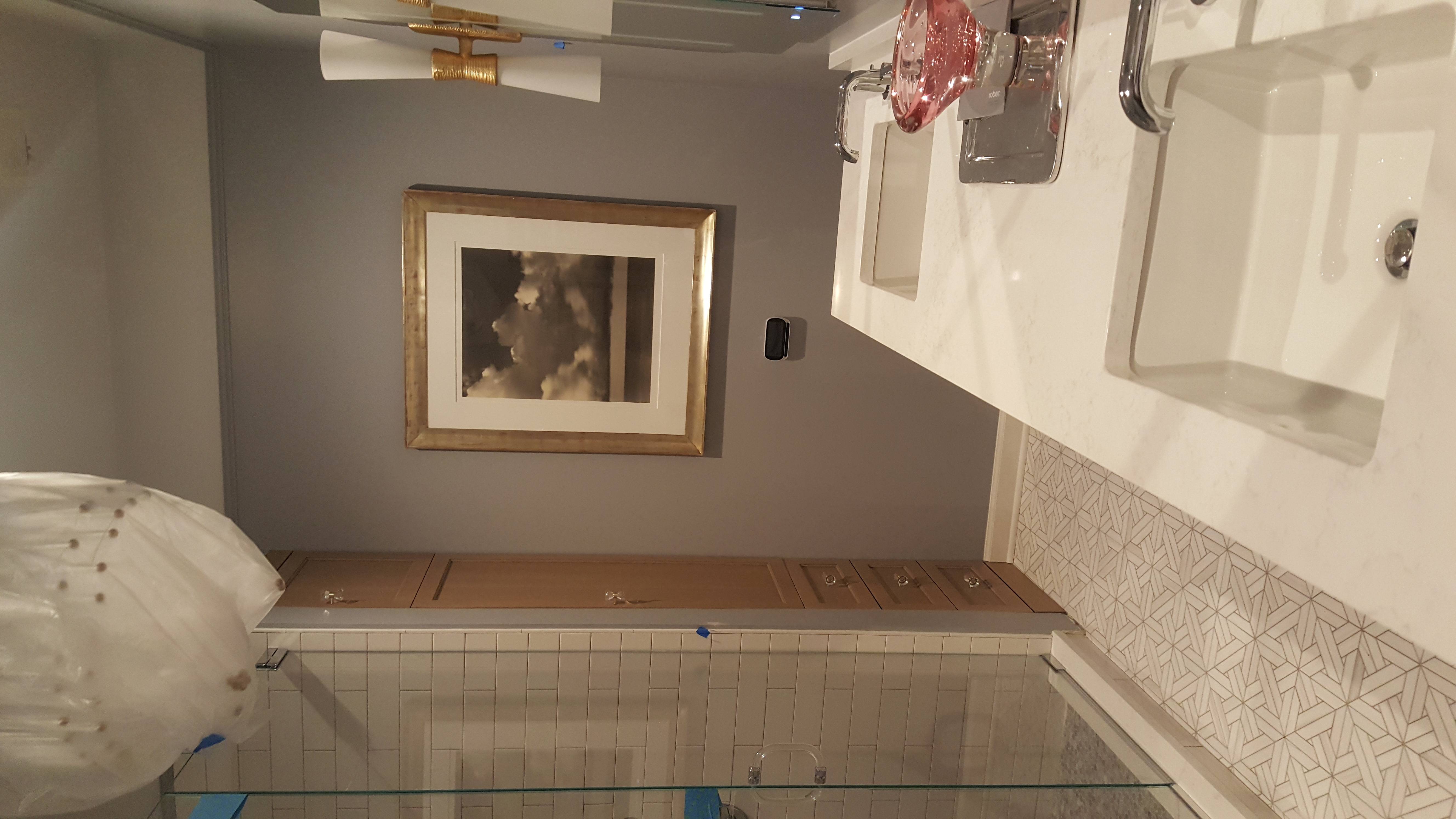 Elegant master bath with double undermount sinks, quartz countertop, glass shower with white subway tile, oak built-in storage, geometric mosaic floor, and gold sconce lighting by Chris Painting and Remodeling.