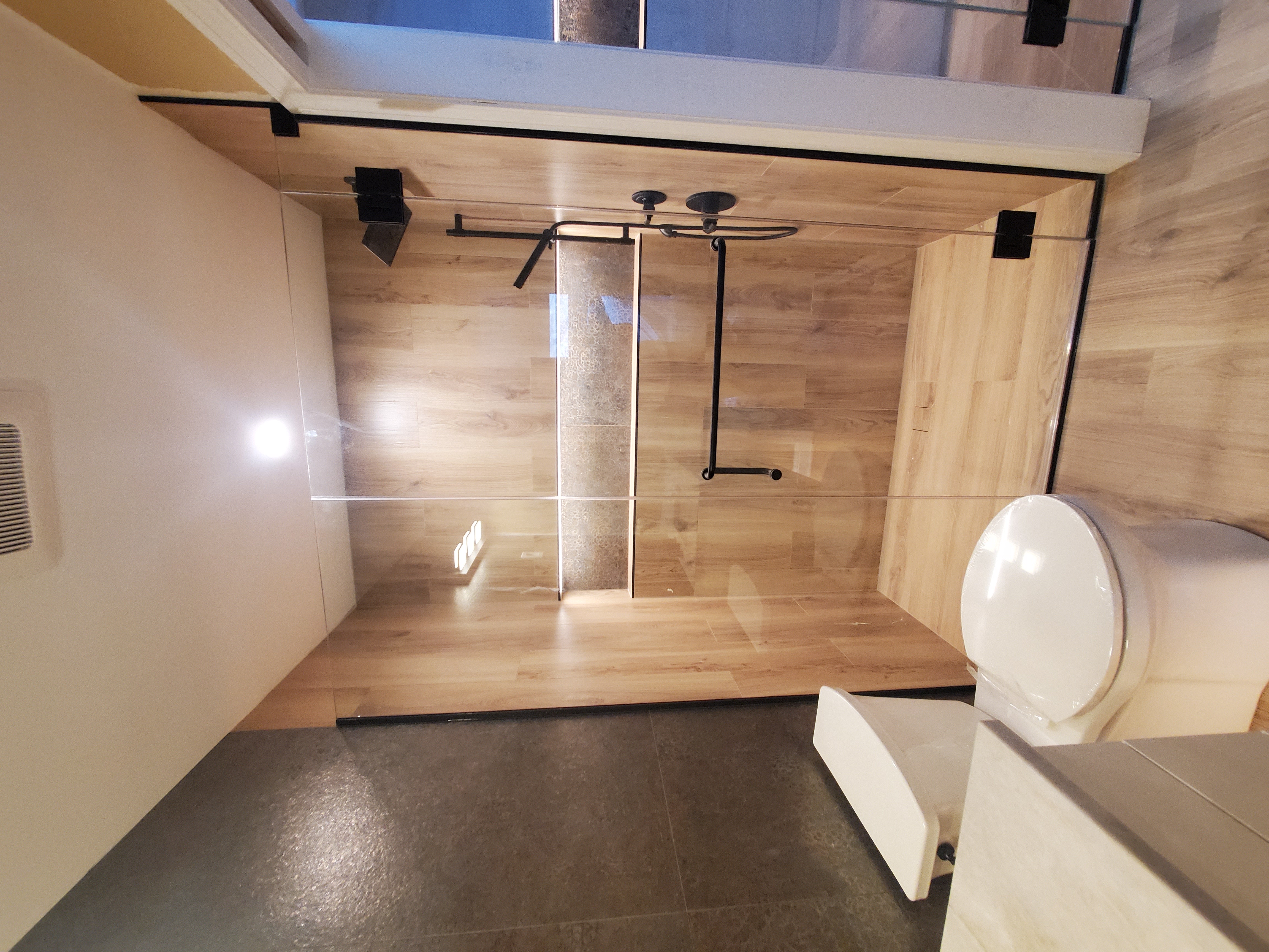 Modern walk-in shower with wood-look plank tile surround, frameless glass door with black hardware, LED-lit recessed niche, and dark accent wall installed by Chris Painting and Remodeling.