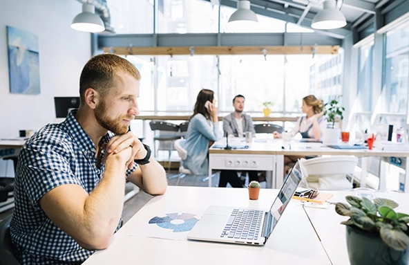 A professional reviewing analytics data on a laptop in a modern open office setting, demonstrating Performance Marketing Agency Services.