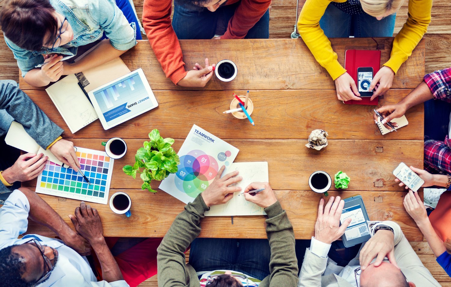 Creative team collaborating at a wooden desk with campaign charts and color swatches to evaluate Marketing Agency Cost.