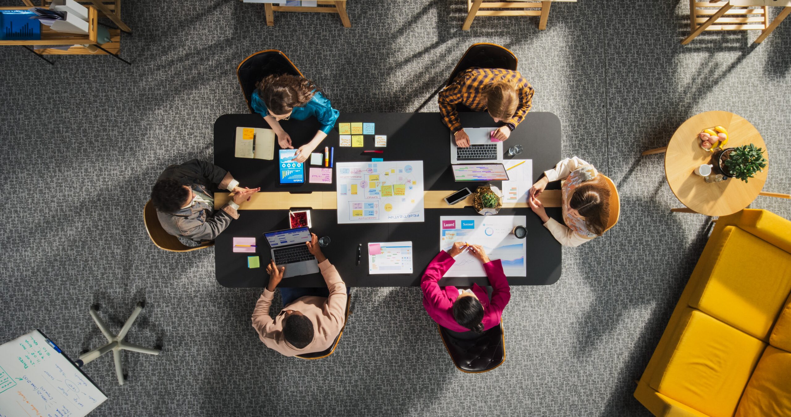 Top-down view of a team collaborating with laptops and planning documents around a conference table, illustrating the strategic balance of choosing a Marketing Agency vs In House team.