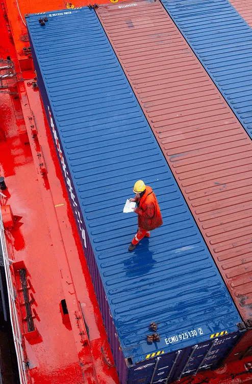 Image of dockworker on top of shipping containers