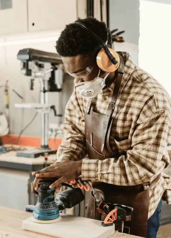 Craftsman using a power sander on wood in workshop, illustrating equipment usage for business efficiency and asset management.