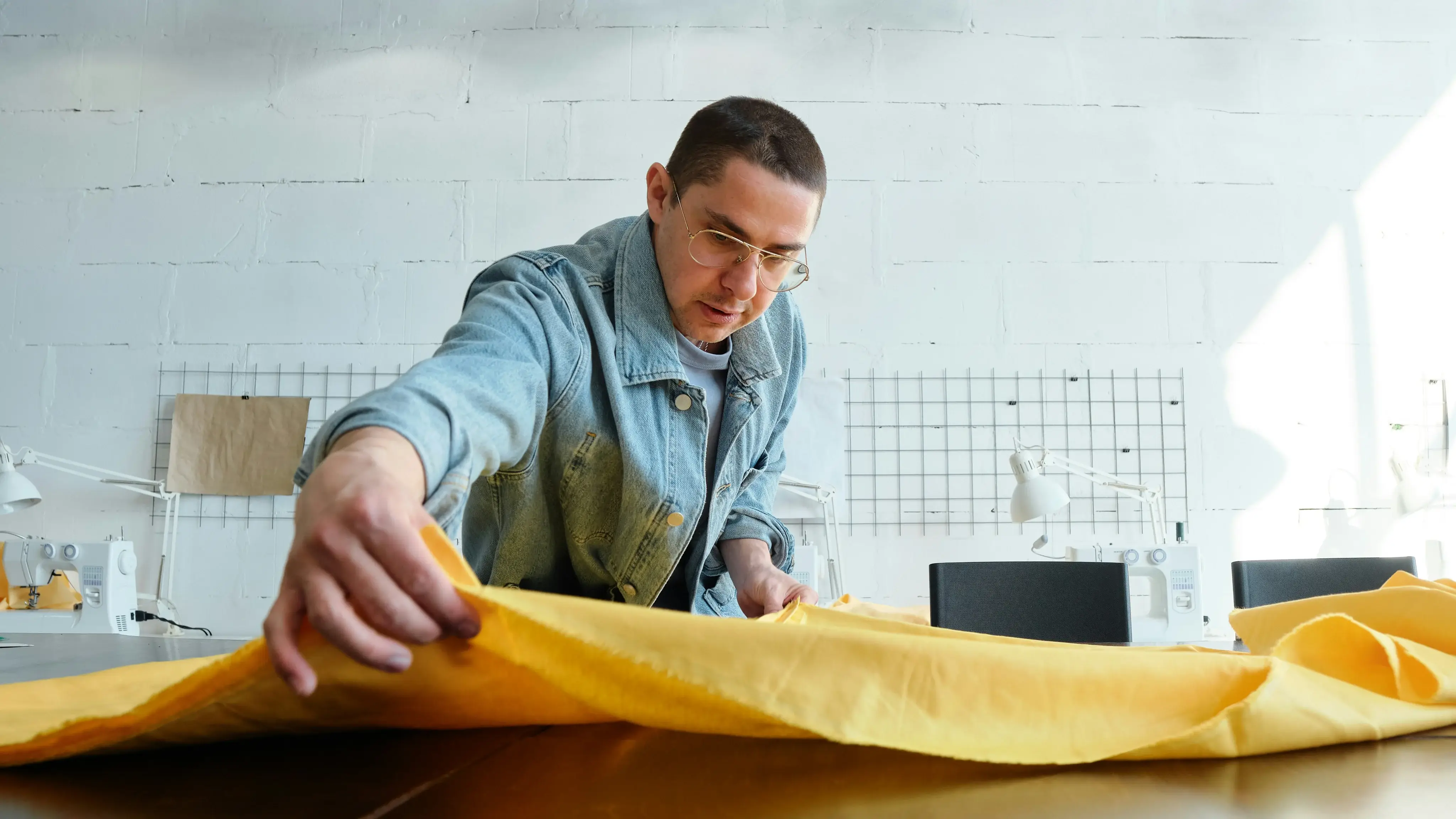 Maker smoothing out a length of yellow fabric on a cutting table in a sewing studio