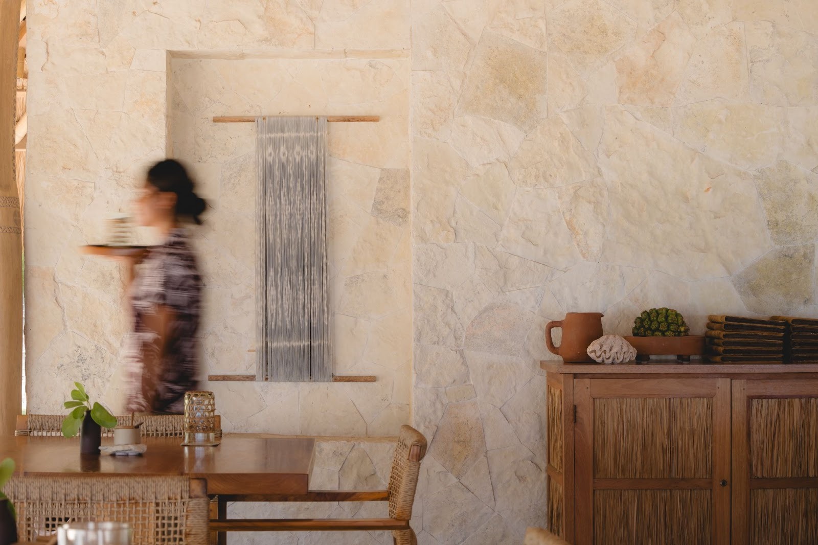 Waitress carrying drinks inside a rustic tropical restaurant.