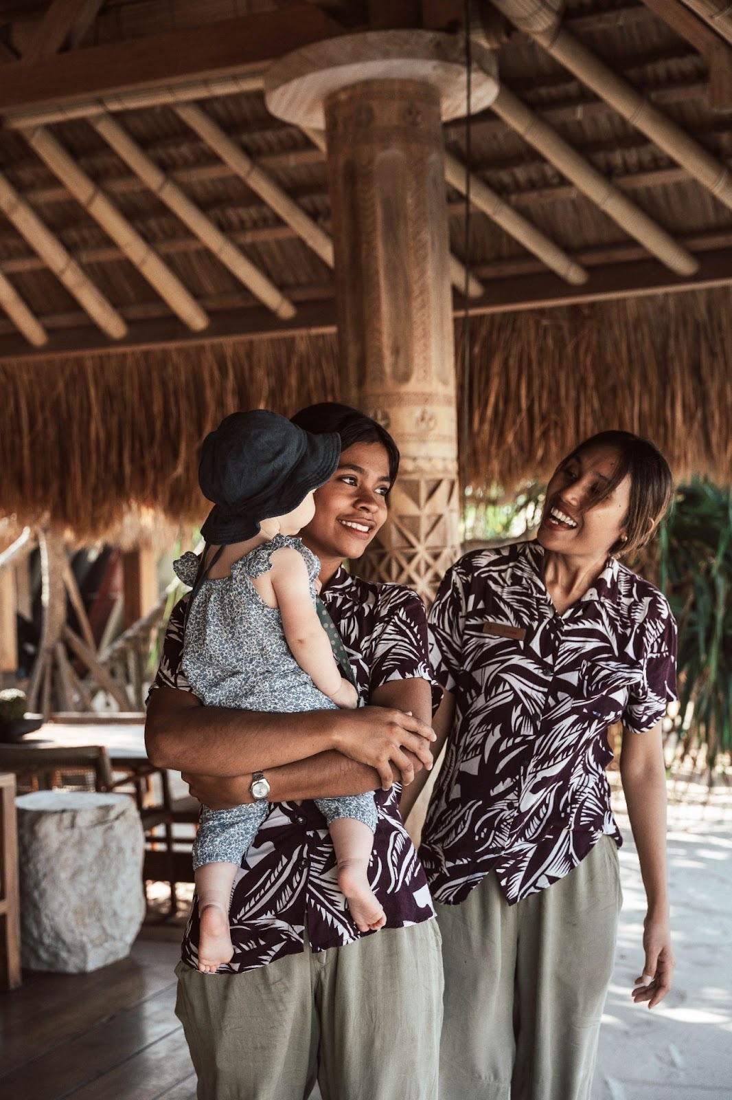 Two smiling staff members holding a baby at a tropical resort