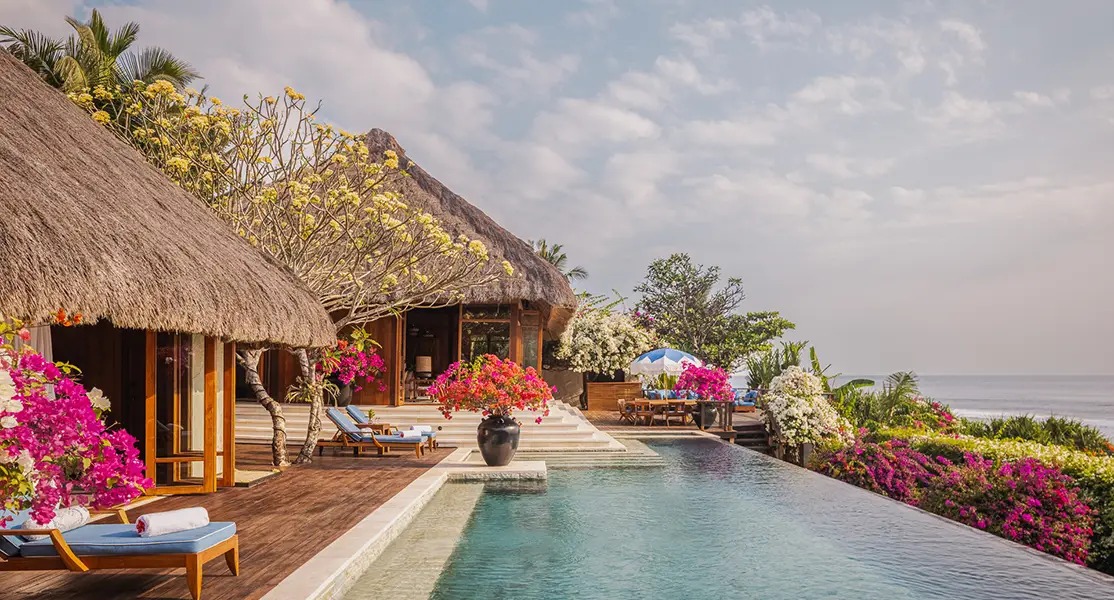 Thatched-roof villa at Nihi Sumba featuring an infinity pool and vibrant tropical gardens overlooking the ocean.