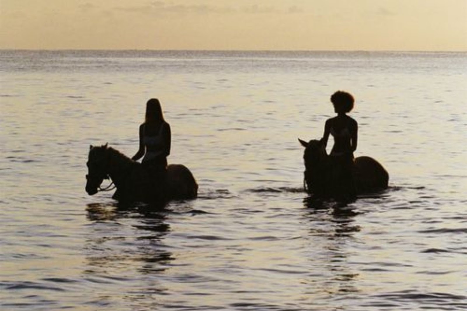 Two women are horseback riding in the shallows