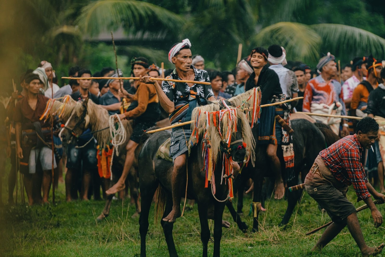 Mounted Pasola warriors holding wooden spears surrounded by local spectators in a West Sumba village