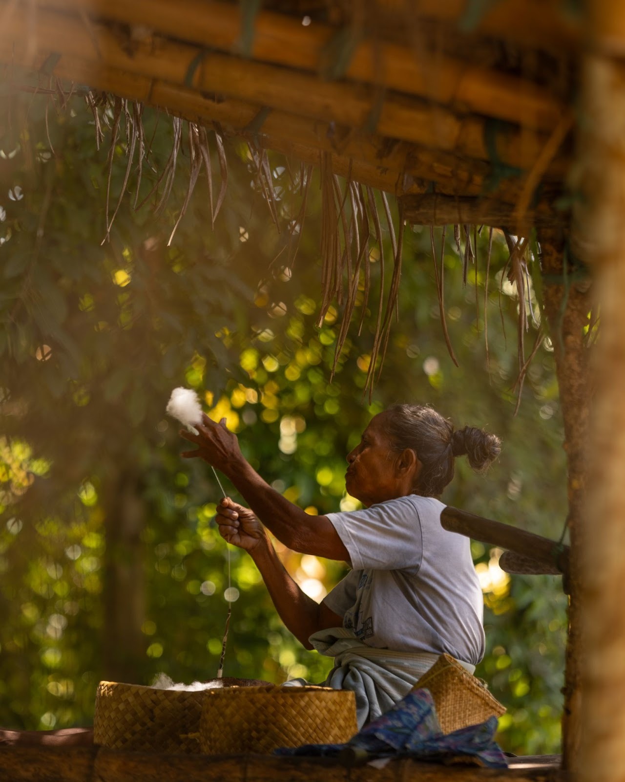 Sumbanese woman preparing natural fibers for traditional ikat weaving under a village hut in West Sumba