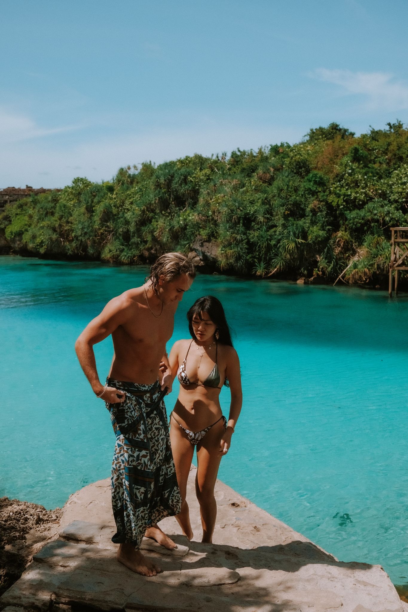 Couple standing at the edge of Weekuri Lagoon natural saltwater pool enclosed by limestone karst in West Sumba Indonesia — day excursion from Sumba paradise resort