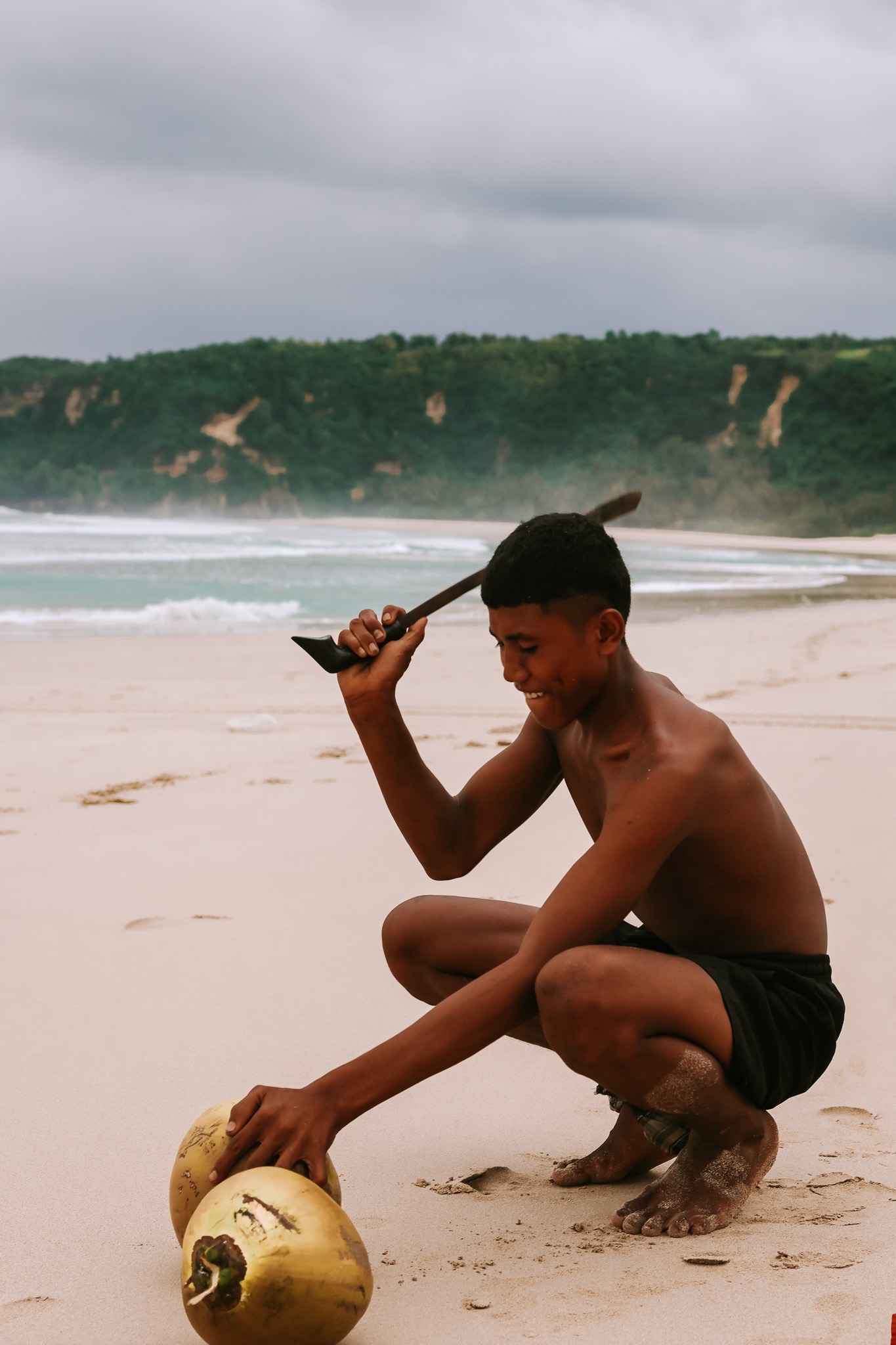 Young Sumbanese man opening a coconut with a traditional blade on a white sand beach in West Sumba Indonesia near The Sanubari Sumba