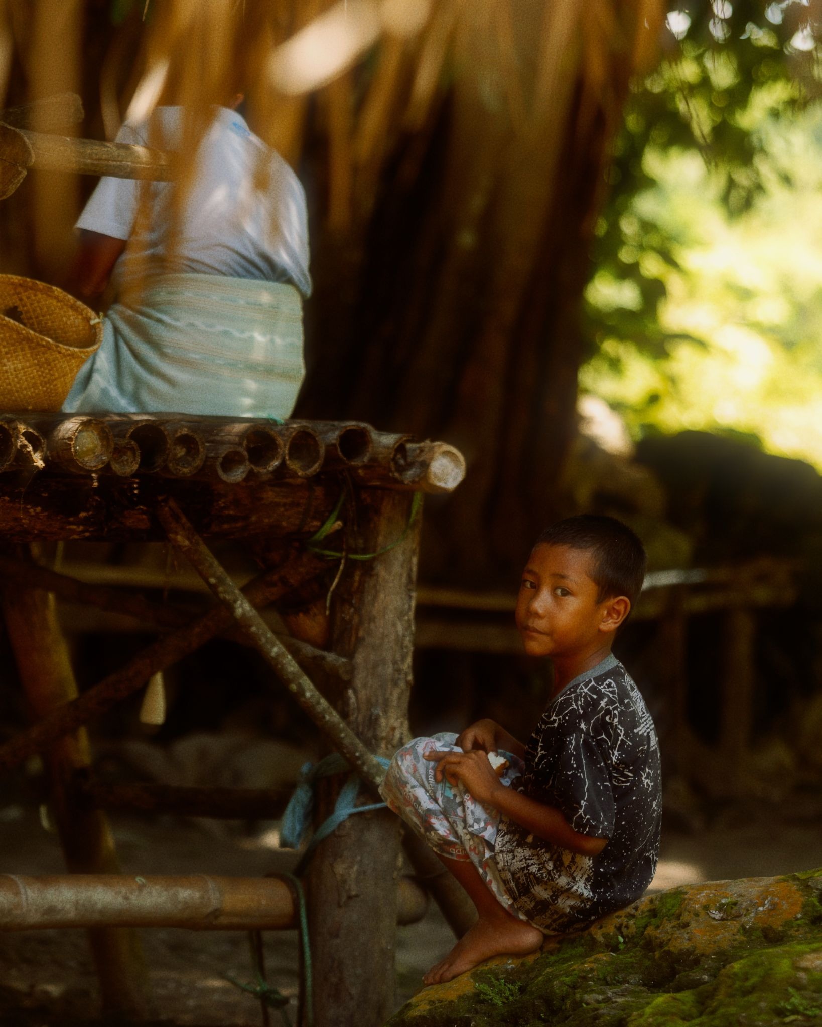 Young Sumbanese boy sitting under a traditional thatched structure in a rural village in West Sumba Indonesia near The Sanubari Sumba resort