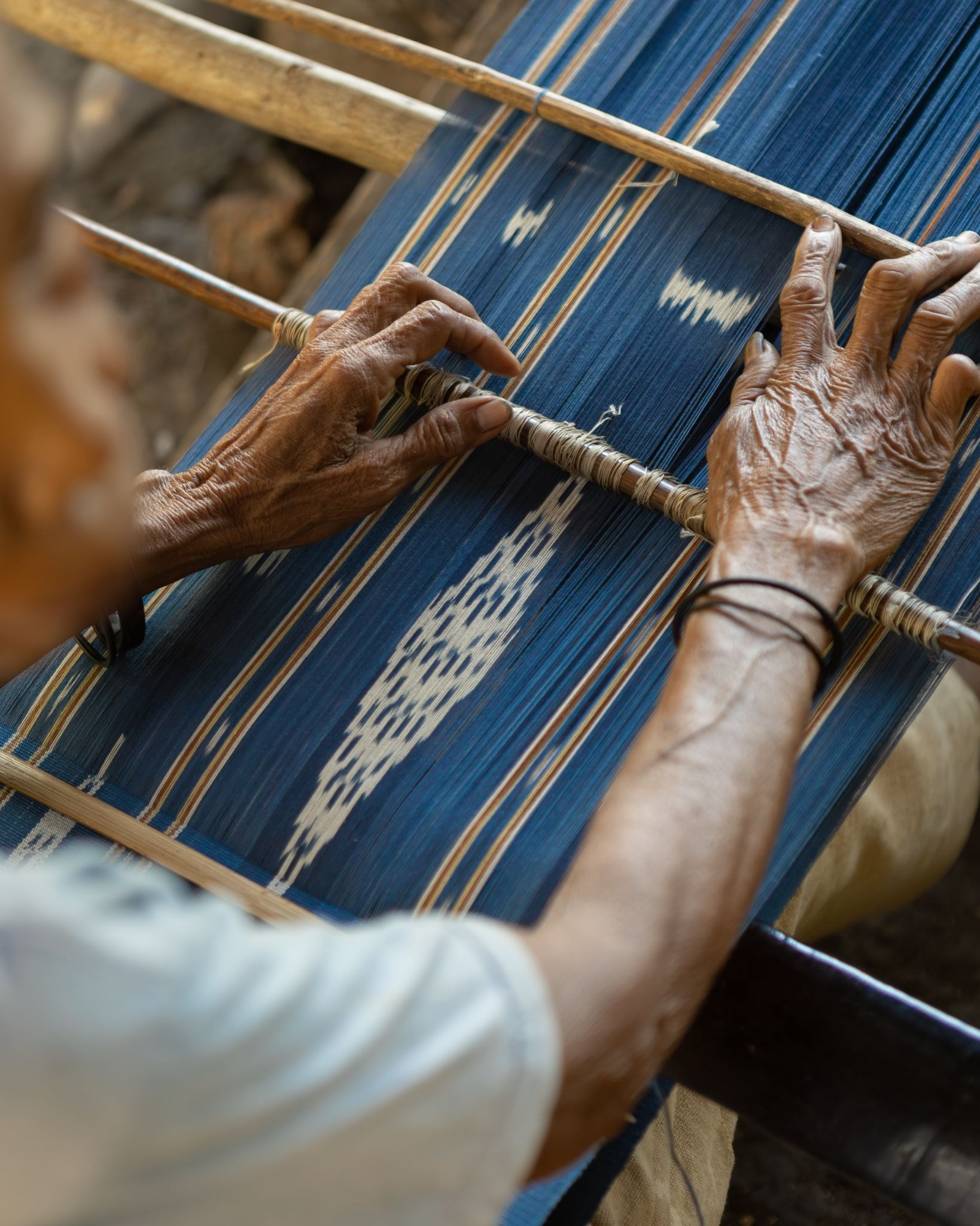 Close-up of a local Sumba artisan's hands weaving naturally dyed blue ikat textile on a traditional wooden loom.
