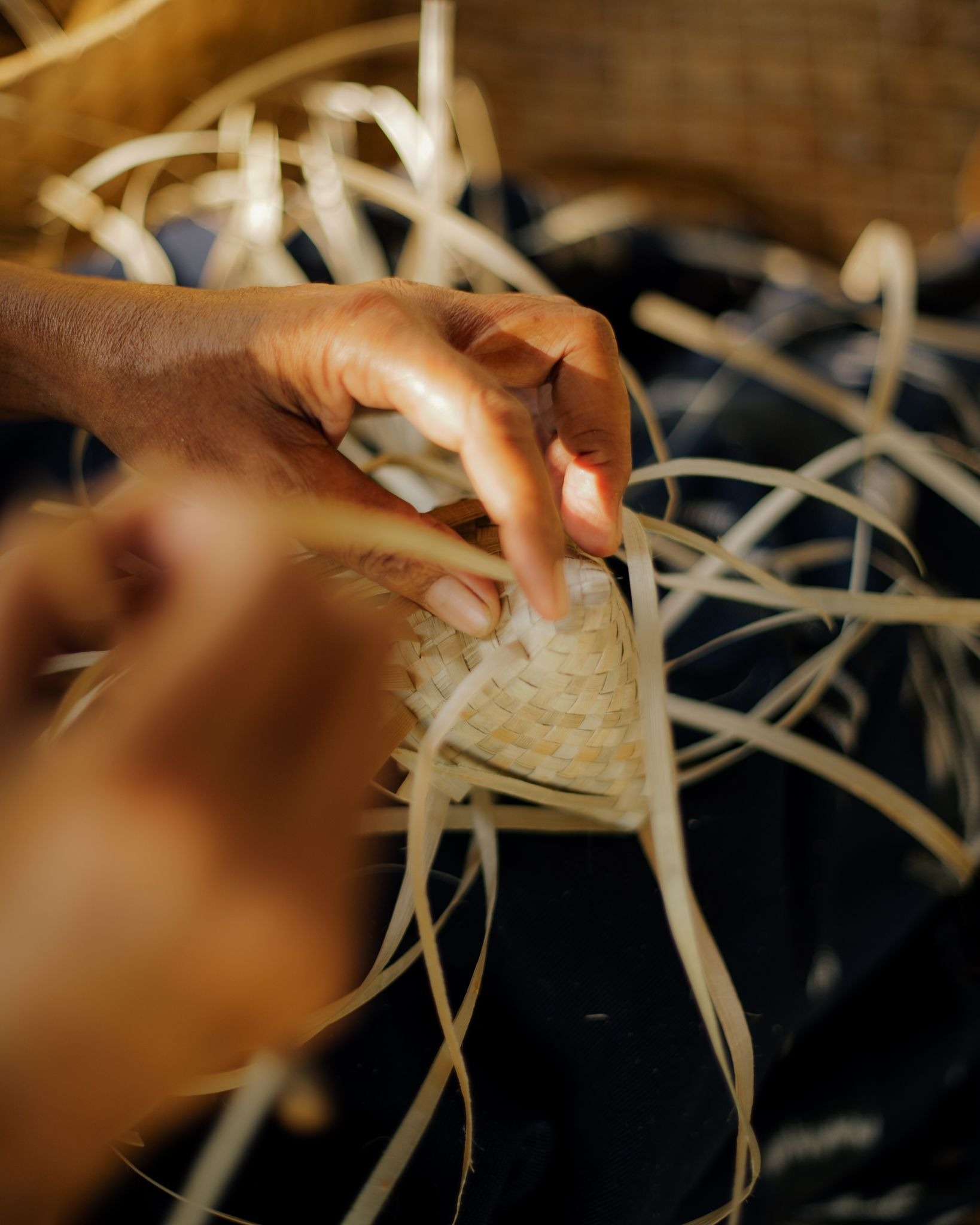 Close-up of an artisan's hands carefully weaving dried pandan and palm leaf fibers to create a traditional Sumbanese basket.