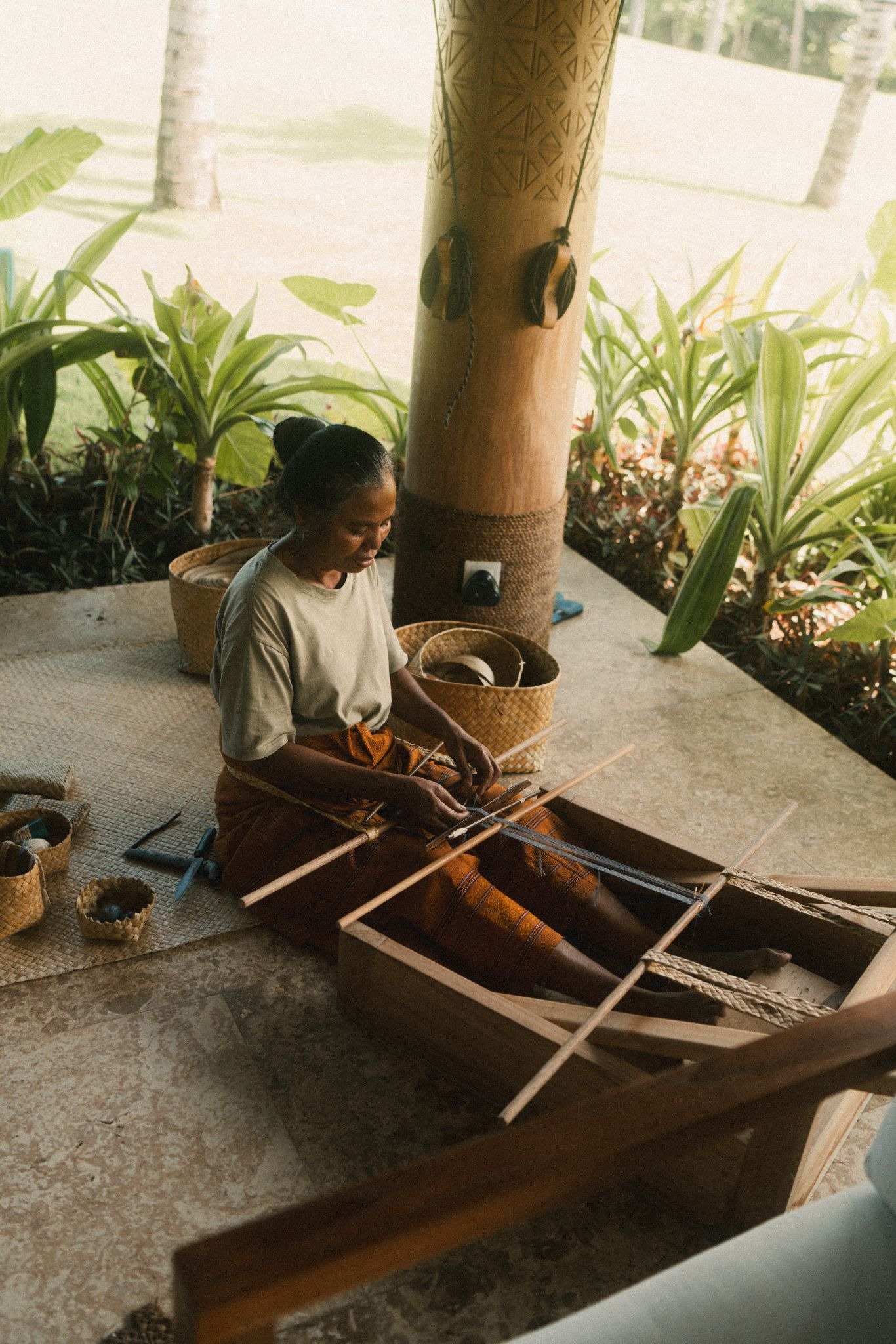 A local Sumbanese woman demonstrating traditional backstrap loom weaving at The Sanubari Hotel Boutique Sumba, surrounded by handcrafted pandan baskets
