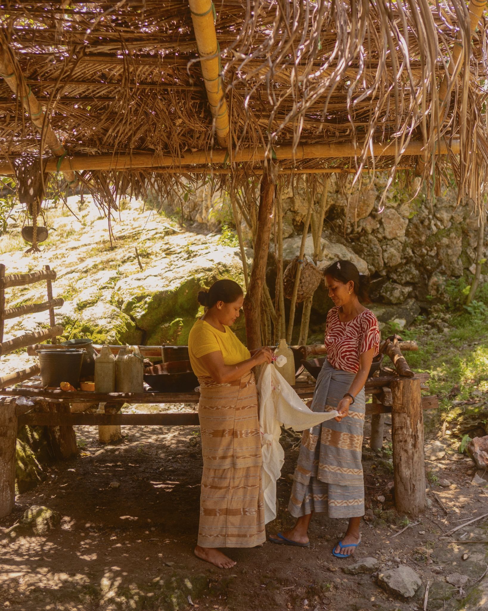 Two Sumbanese women in ikat sarongs preparing cloth at a traditional village weaving station