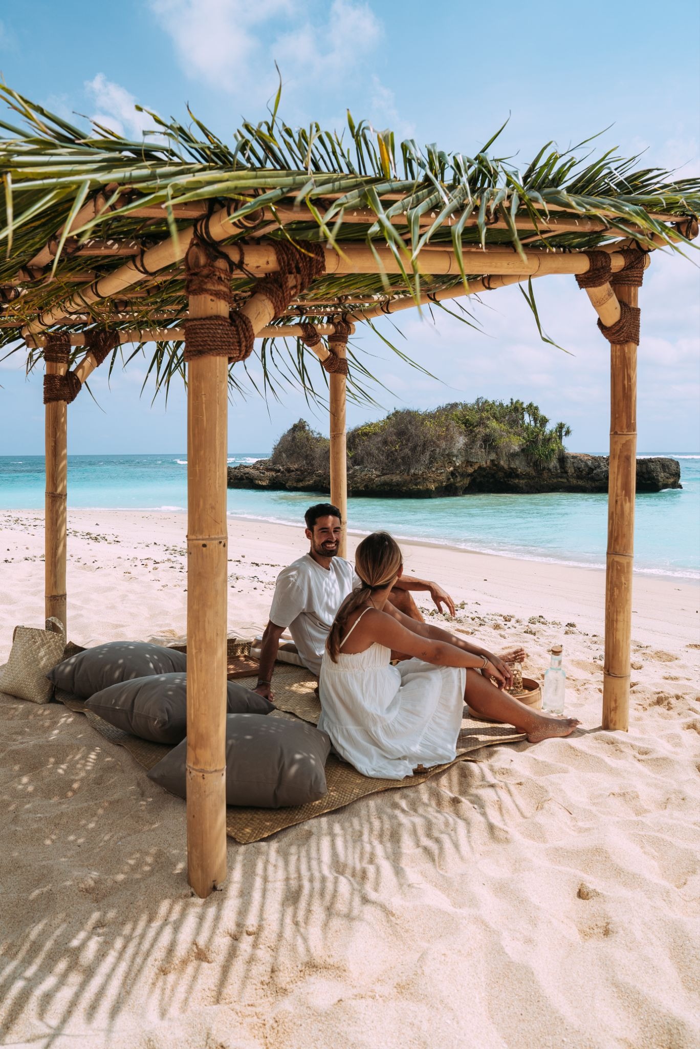 Couple enjoying a private beach picnic at The Sanubari, a luxury Sumba Island hotel with a bamboo cabana overlooking West Sumba's secluded white sand beach.