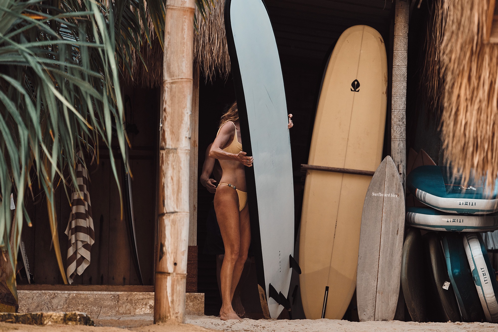 Surfer walking into the ocean with a stand-up paddleboard at sunset on a Sumba beach