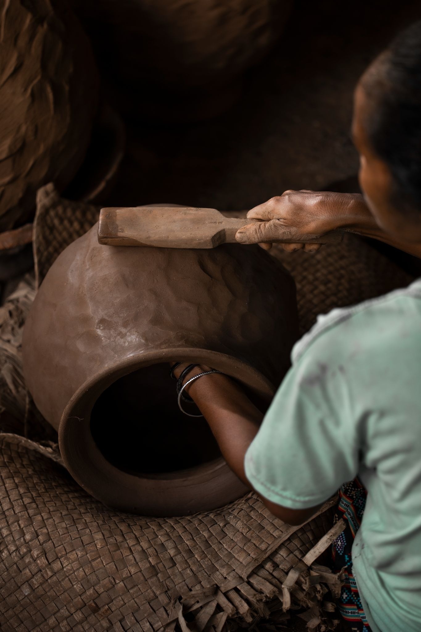 A Sumbanese artisan using a wooden paddle tool to shape and smooth a large clay vessel.